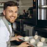 man baker puts croissants dough into oven
