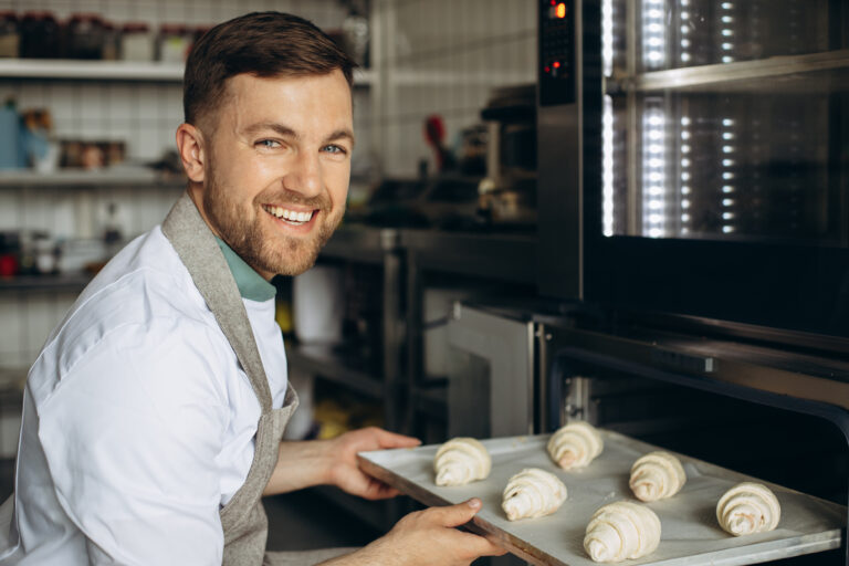 man baker puts croissants dough into oven