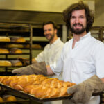 smiling baker carrying tray freshly baked french baguette