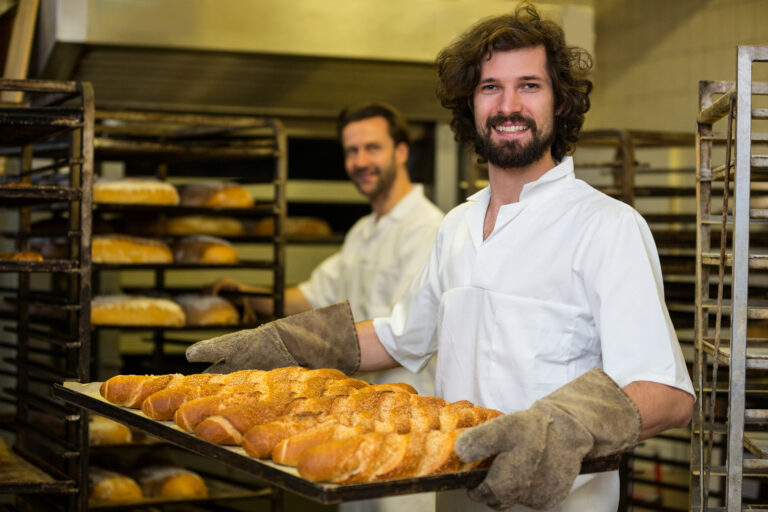 smiling baker carrying tray freshly baked french baguette