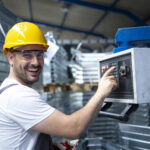 portret pracownika fabryki obslugujacego maszyne przemyslowa i ustawiajacego parametry na komputerze